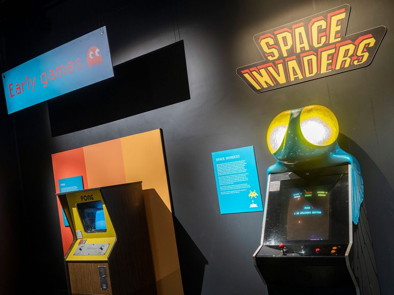 Two arcade games side by side in the Game On exhibition. One is Space Invaders, the other is Pong.