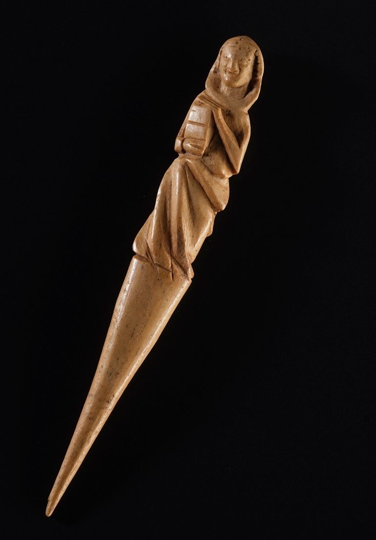 A wooden pointed hair parter, with a triangular pointed and a a mother and child carved into the top.