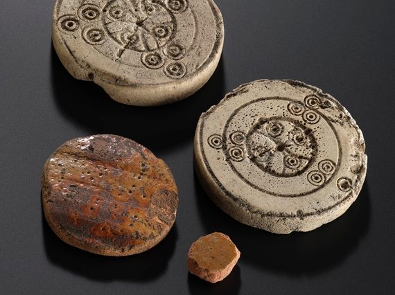 4 circular playing pieces against a black background. 2 are made from pottery, whilst 2 are from bone - and on them has been etched a circular pattern.