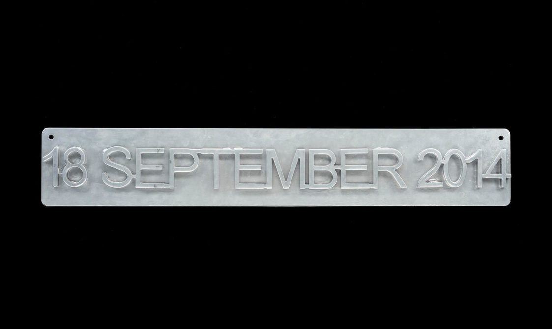Grey steel sign rectangular and narrow with slightly rounded corners viewed straight on, with raised text across it reading '18 SEPTEMBER 2014'.