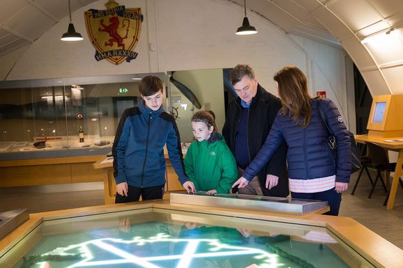 A family of four interacts with a light map of the East Fortune airfield in the Fortunes of War gallery.