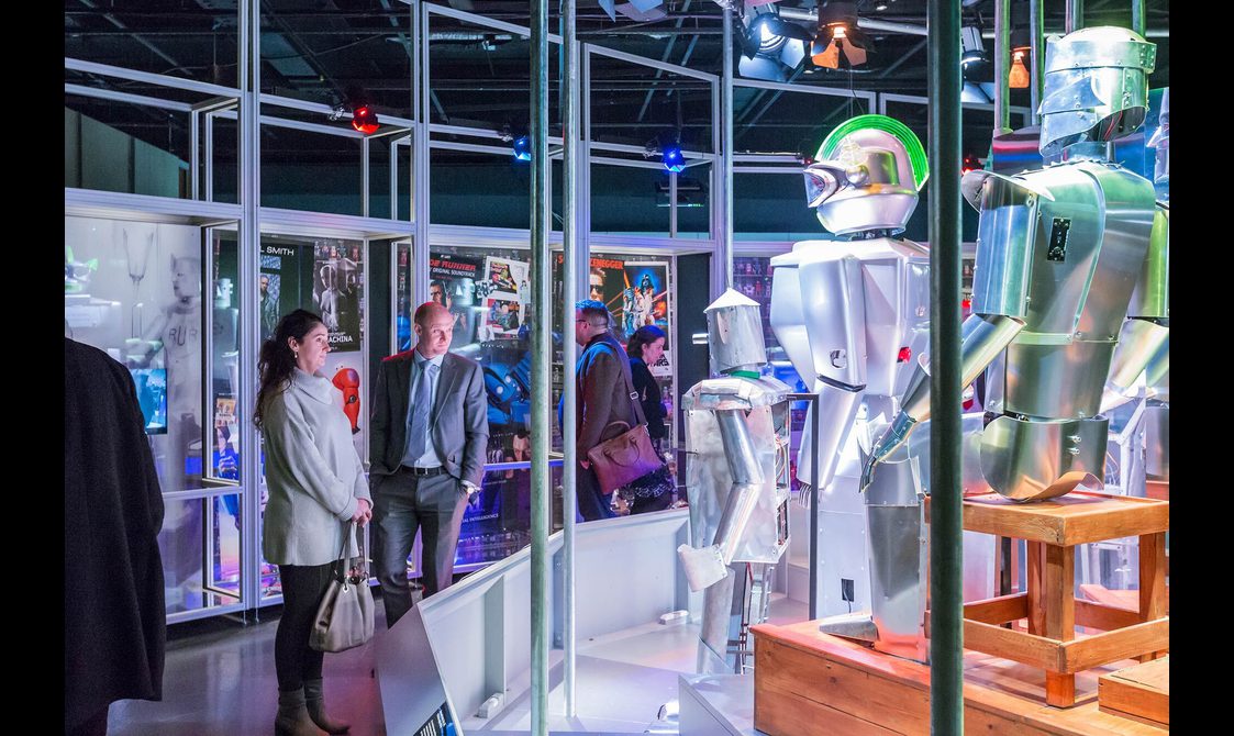 Visitors looking at robots on display in a museum case in the Robots exhibition.