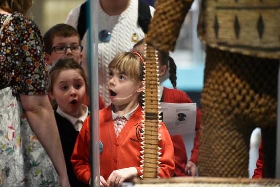 Children with shocked looks on their faces standing in front of museum objects.