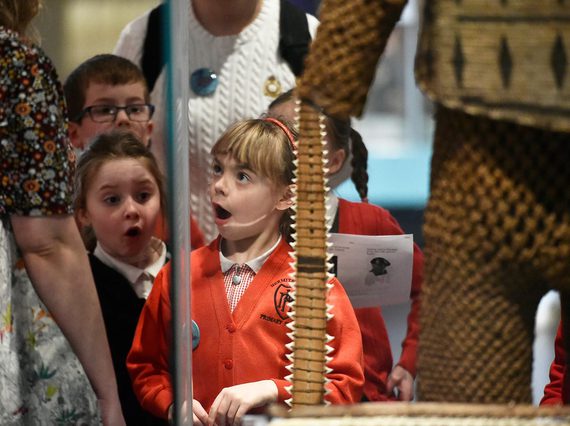 Children with shocked looks on their faces standing in front of museum objects.