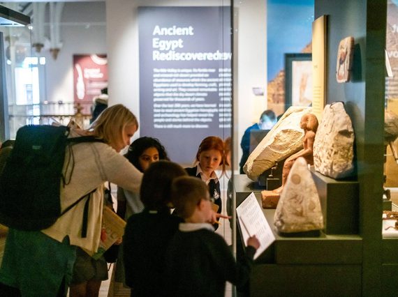 A teacher gathers a group of primary pupils around one of the cases in the Ancient Egypt Gallery.