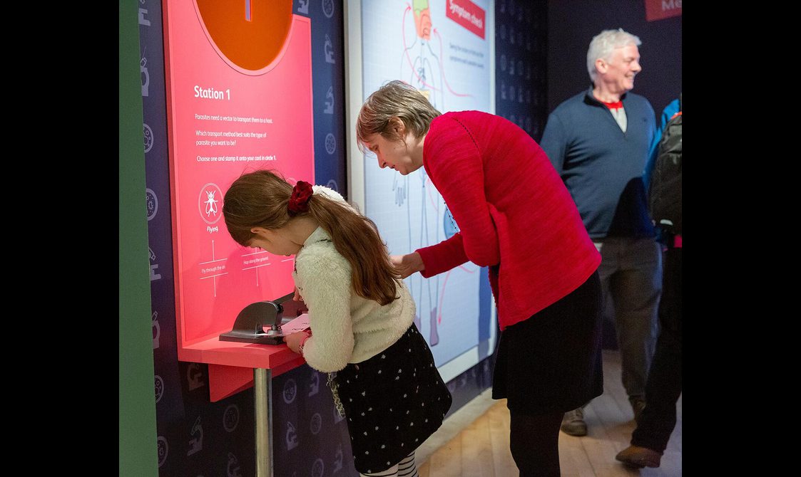 A child using a stamp press on a piece of card next to an adult who is supervising them.