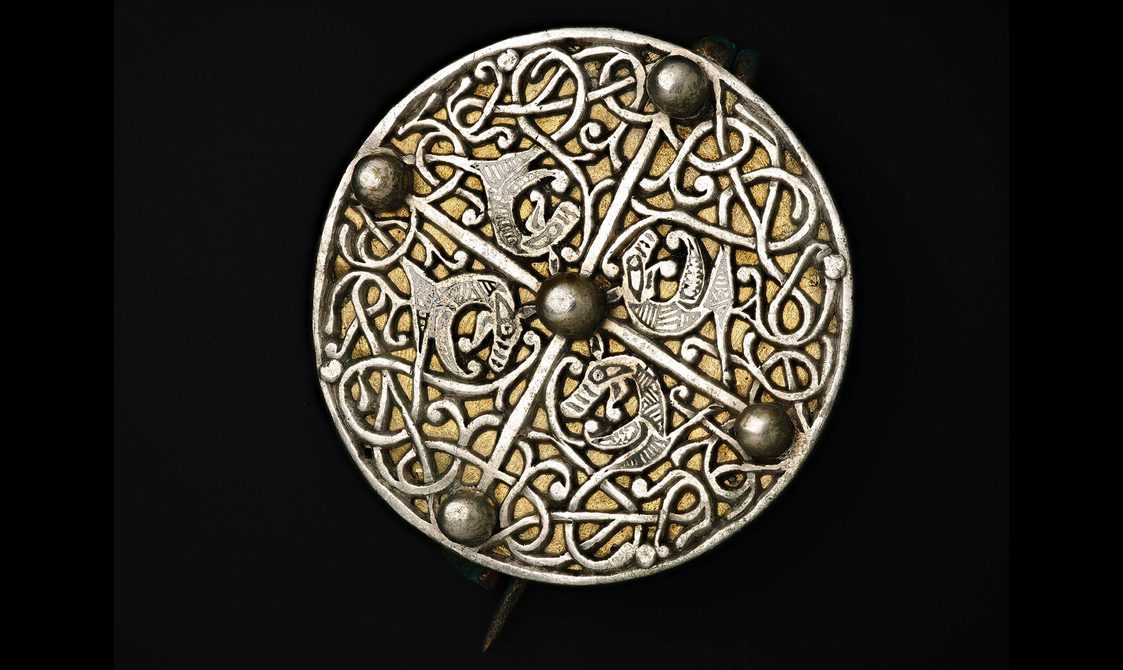 A circular broach engraved with weaving Anglo-Saxon designs.