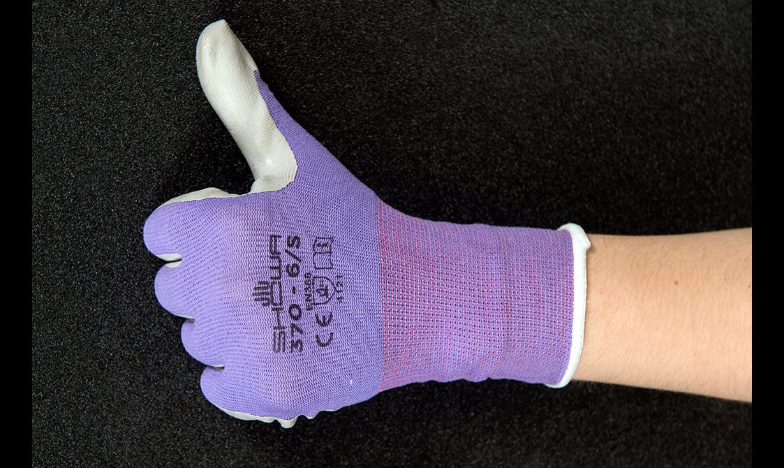 Close up of a hand wearing purple heavy duty work gloves giving a thumbs up.