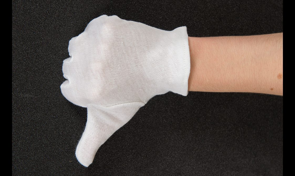 Close up of a hand wearing a white cotton glove giving a thumbs down.