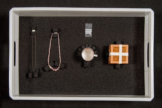 Two necklaces, a ring, a mug, and a wooden box packed in a plastic box with foam blocks.