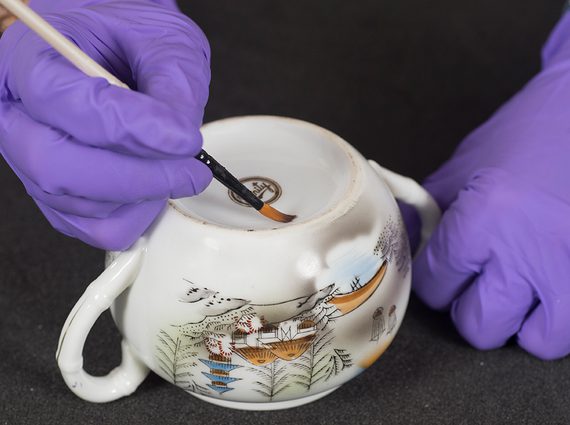 A curator applying a reference label to a ceramic cup.