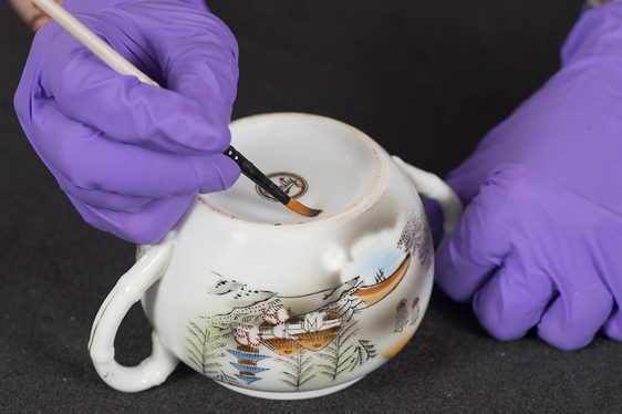 A curator applying a reference label to a ceramic cup.