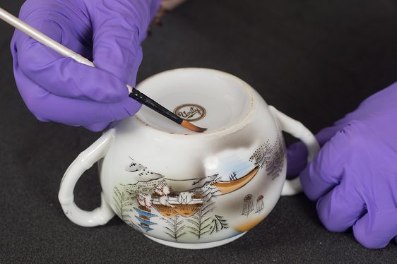 A pair of gloved hands applying a label to a ceramic pot.