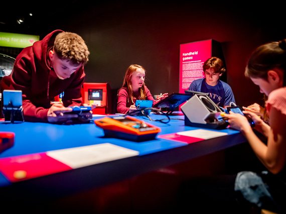 4 young visitors are playing on handheld games in an exhibition space.