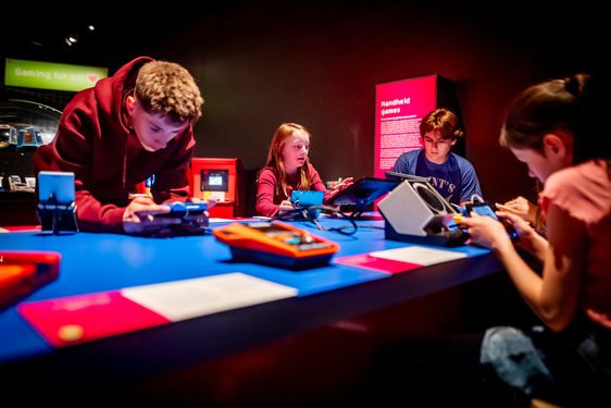 4 young visitors are playing on handheld games in an exhibition space.