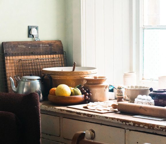 A kitchen countertop next to a window. Baking utensils sit on the countertop next to a fruit bowl.