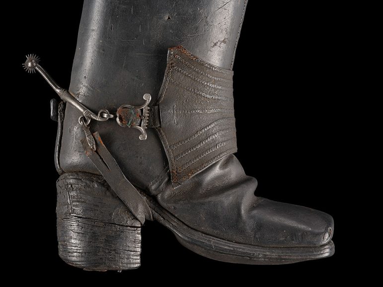 Side angle of a 17th century Jack boot propped up against a black background.