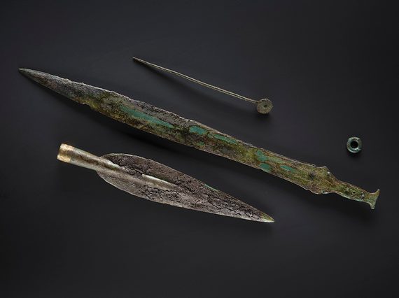 A Bronze Age sun headed pin, sword and spearhead. The remnants of a wooden scabbard are laid on the sword.