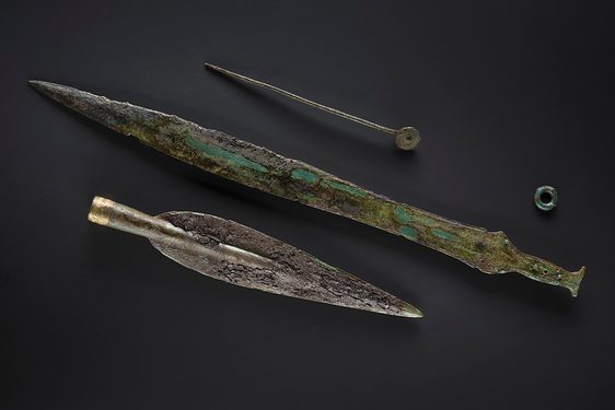 A Bronze Age sun headed pin, sword and spearhead. The remnants of a wooden scabbard are laid on the sword.