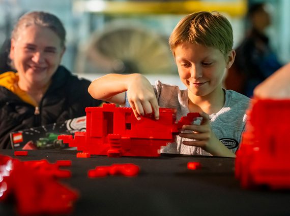 A parent and child play with red Lego bricks on a table.