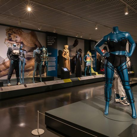 Thirteen mannequins arranged in exhibition, with blue blackdrops.