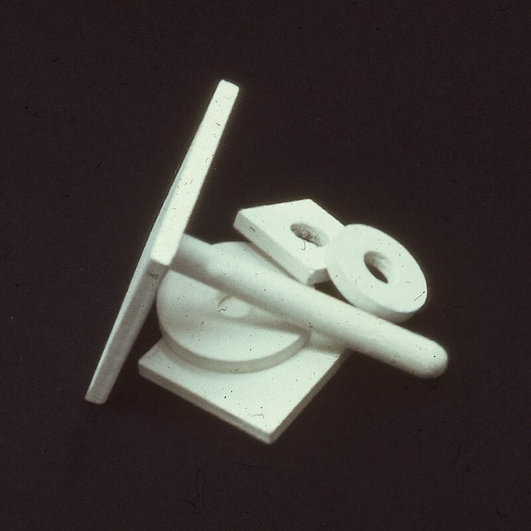 A colour photograph of some white 3-dimensional objects piled on top of each other against a black background. The objects include shapes like flat doughnut rings and a a post mount on its side, a flat square with a small pole sticking out of it at a 90 degree angle.
