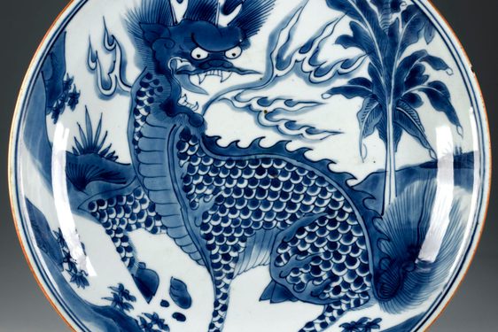 Circular plate with a blue dragon figure in the center wit ha palm tree and landscape scenery in the background.