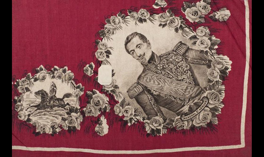 Two fabric samples of a horse rider and a man dressed in military uniform set in a corner of a red fabric