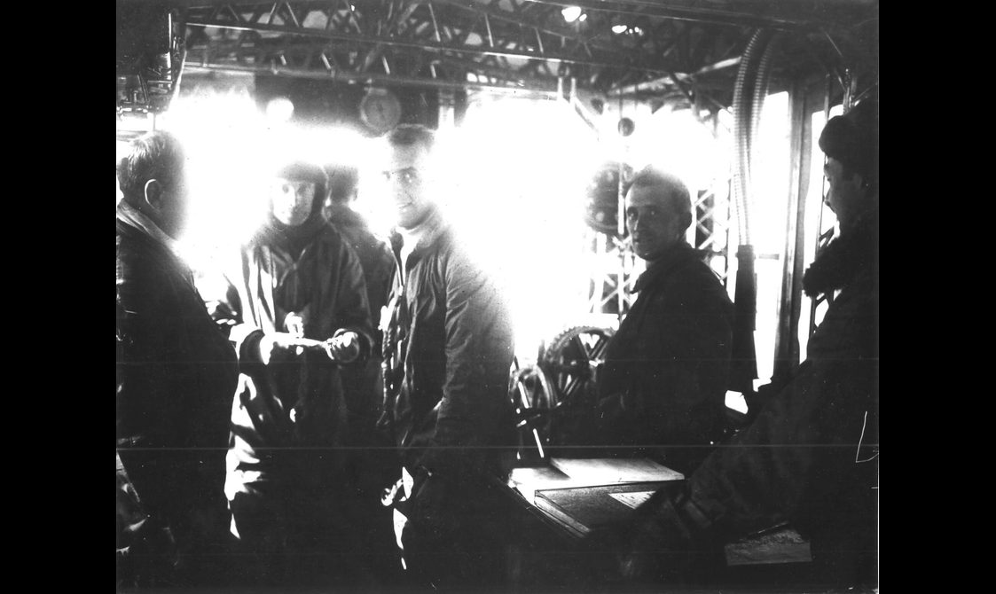 A black and white image of a group of men in the control car of a large airship.