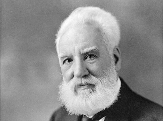A black and white photo of a man with white hair and a beard shown from the waist up. He is wearing a white shirt and a dark waistcoat, jacket, and tie