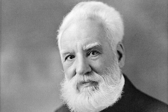 A black and white photo of a man with white hair and a beard shown from the waist up. He is wearing a white shirt and a dark waistcoat, jacket, and tie