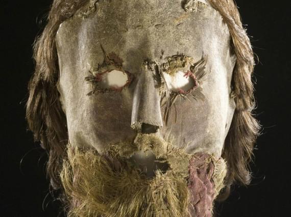 A leather mask with openings for eyes with a long brown wig and beard attached.