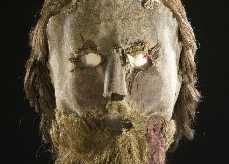 A leather mask with openings for eyes with a long brown wig and beard attached.