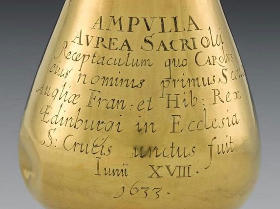 A close up or a rain drop shaped gold vessel with inscribed Latin lettering.