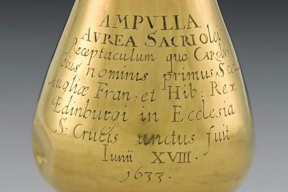 A close up or a rain drop shaped gold vessel with inscribed Latin lettering.