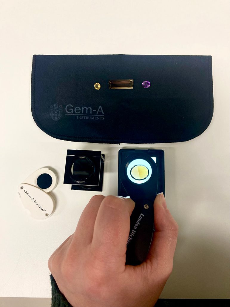 An amber-coloured gem being examined under a handheld lens