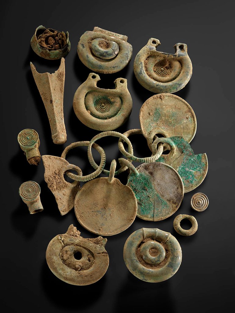 Twelve bronze objects, including some rounded fittings with concentric circle designs and a rattle pendant.
