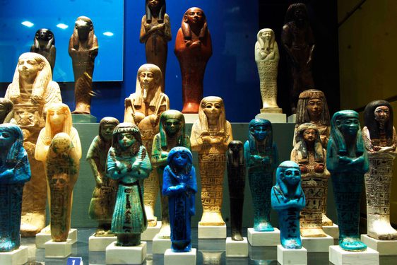 A variety of small Ancient Egyptian statues of humans with arms crossed.