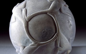 The bottom of a bowl carved from a grey stone with a pattern of connected baboons