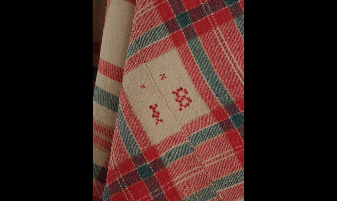 Detail of a red, green, and cream tartan fabric with embroidered initials.