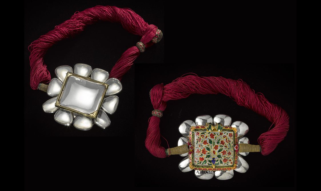 A bracelet with a twisted red fabric band and a large square glass ornament with smaller squares framing it. The reverse of the bracelet is also shown which has a gold back on the square with a pattern in red, green, and blue.
