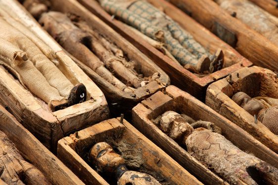 Small figurines of corpses are laying in little wooden boxes, all in a row.