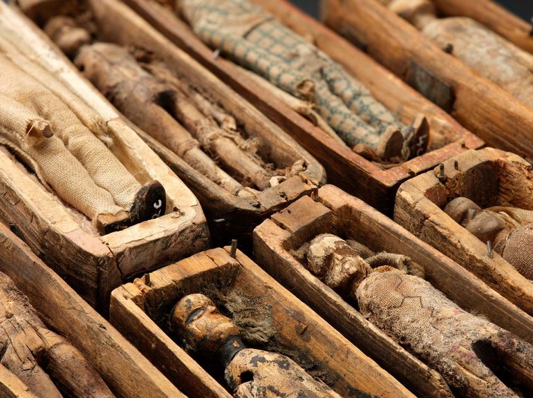 Small figurines of corpses are laying in little wooden boxes, all in a row.
