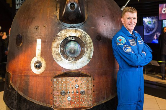 An astronaut in a blue uniform standing next to a spacecraft.