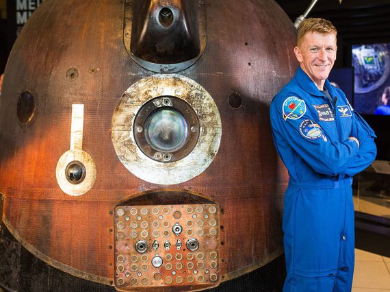 An astronaut in a blue uniform standing next to a spacecraft.