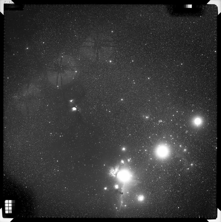 Black and white image of stars on a photographic plate. There are a few very bright spots int he bottom right and scattered points of light around the rest of the image.