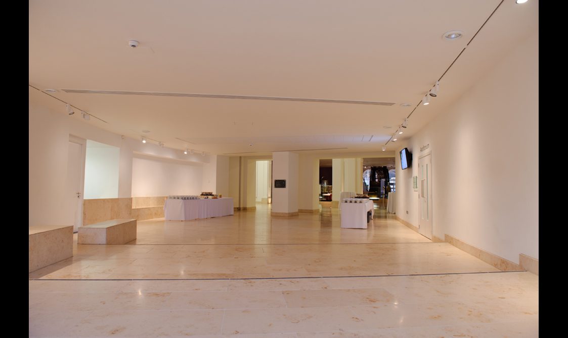 A wide empty space outside an auditorium with white walls and stone floors.