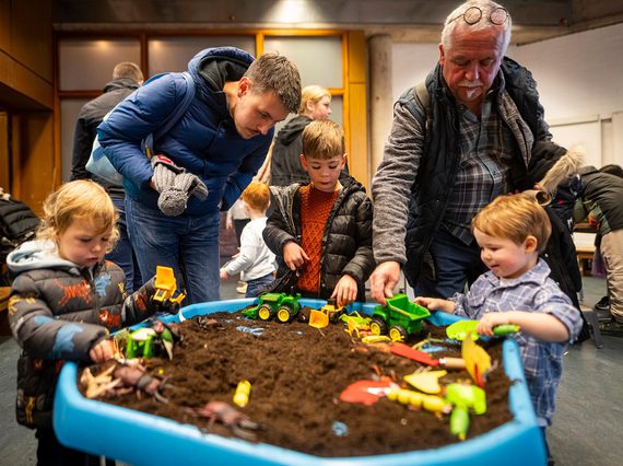 An intergenerational family are playing in a soil pit filled with soil and toy bugs.