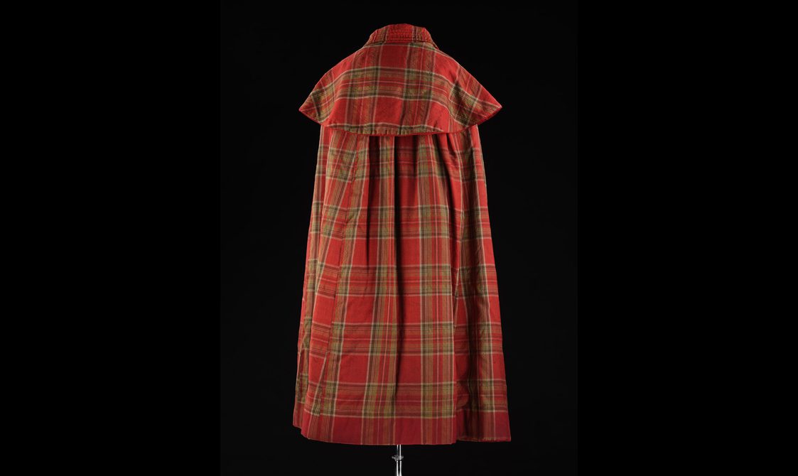 Back view of a mannequin wearing a long red tartan cloak with a large collar