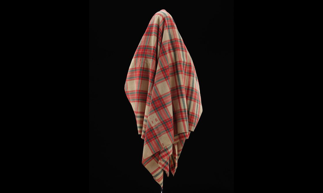 Back view of a mannequin wearing a red and cream tartan shawl.